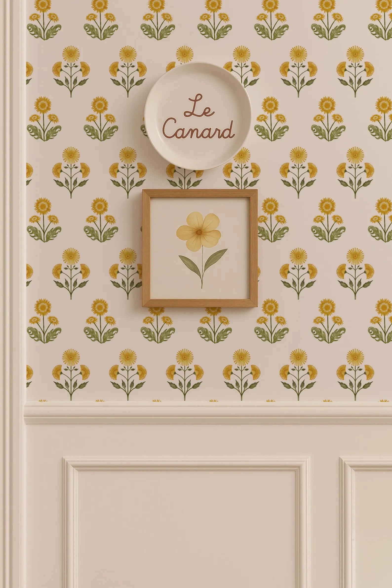 a wall with a floral pattern and a framed picture of a yellow flower. Above the wall, there is a plate with the word "Le Camand" written on it.