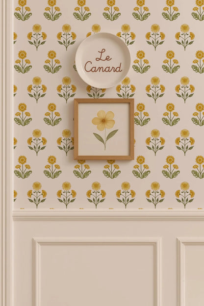 a wall with a floral pattern and a framed picture of a yellow flower. Above the wall, there is a plate with the word "Le Camand" written on it.