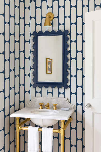 a bathroom with a white sink and gold fixtures, including a mirror and towel rack. The walls are covered in a blue and white geometric pattern, and there is a white door next to the sink.