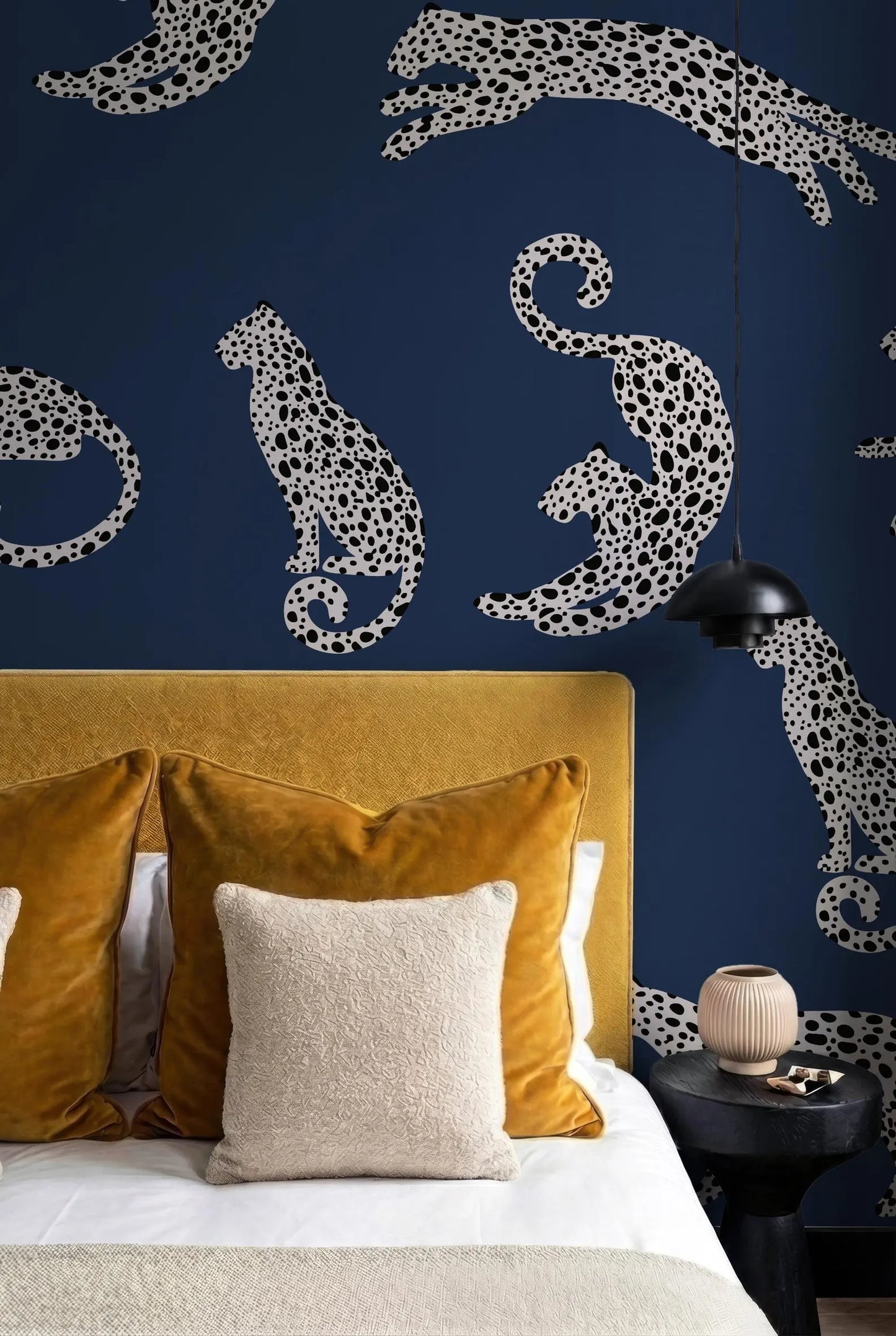 a bedroom with a bed, yellow and beige pillows, and a dark blue wall with a pattern of leopard silhouettes.
