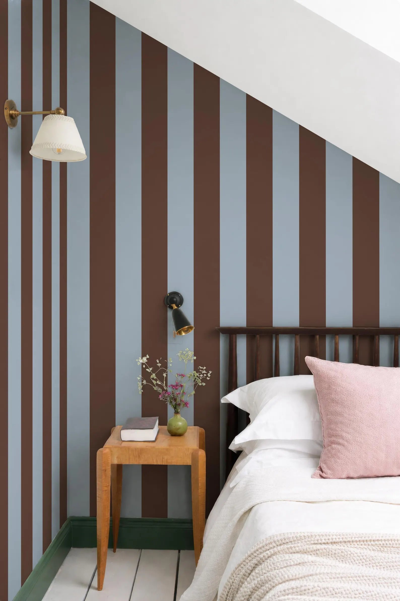 a cozy bedroom with a bed, a wooden nightstand, and a striped wall behind it. The room has a warm and inviting atmosphere, with a mix of brown and blue colors.