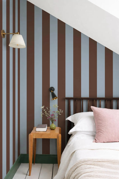 a cozy bedroom with a bed, a wooden nightstand, and a striped wall behind it. The room has a warm and inviting atmosphere, with a mix of brown and blue colors.
