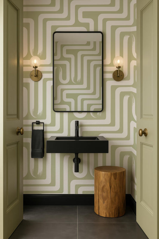 a bathroom with a black sink, a mirror, and two wall sconces. The walls are covered in a green and white patterned wallpaper, and there is a wooden stool in the corner.