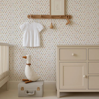 a nursery room with a white dresser, a stuffed duck toy, and a wooden hanger with a white dress hanging on it. The walls are covered in a floral wallpaper, and there is a picture frame hanging on the wall.