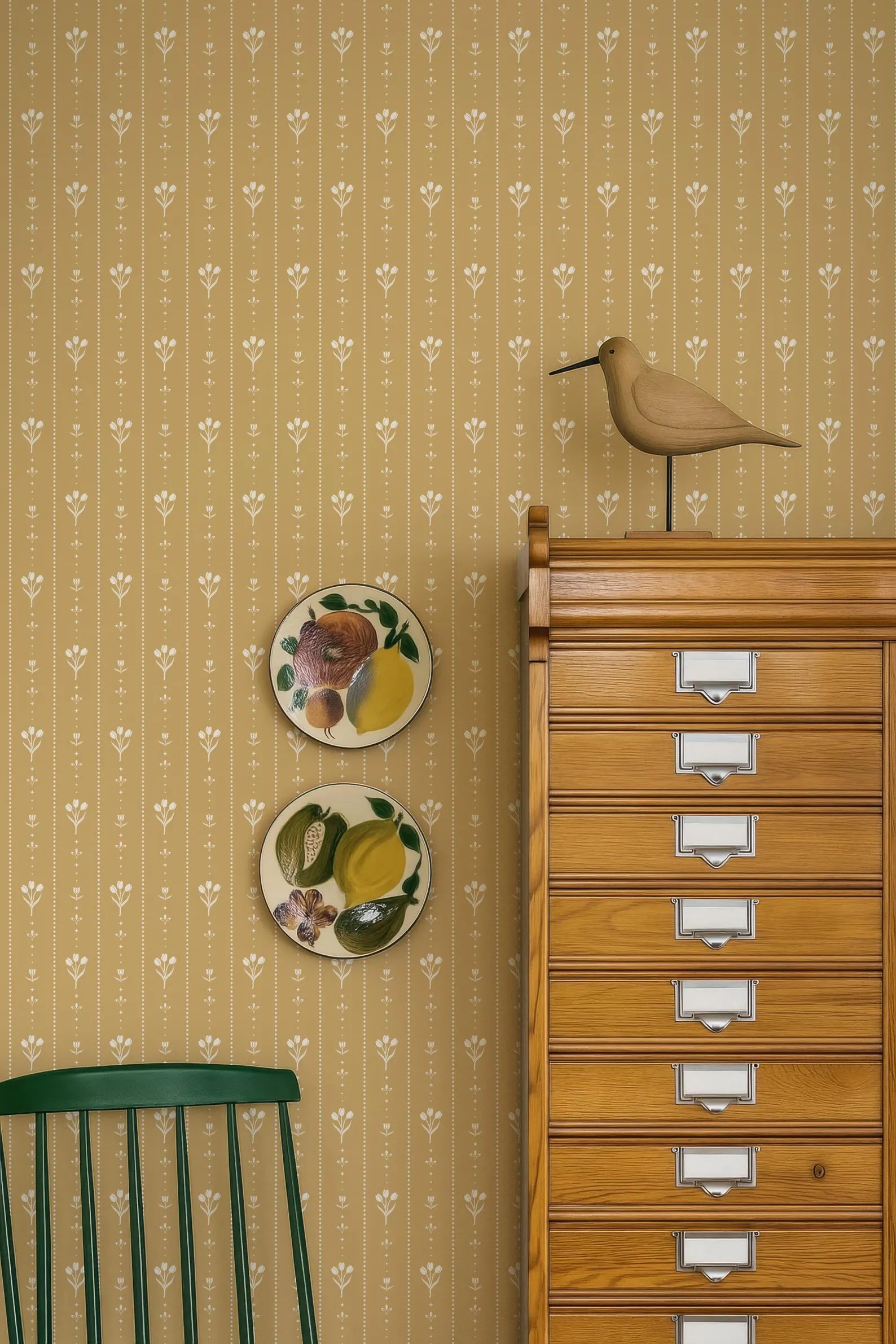 a wooden cabinet with multiple drawers, a green chair, and two decorative plates on the wall.