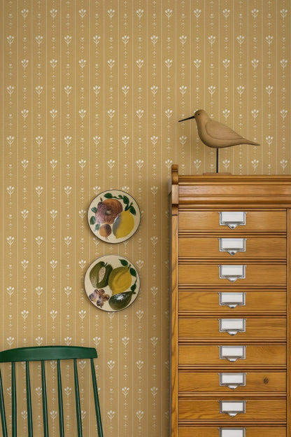 a wooden cabinet with multiple drawers, a green chair, and two decorative plates on the wall.