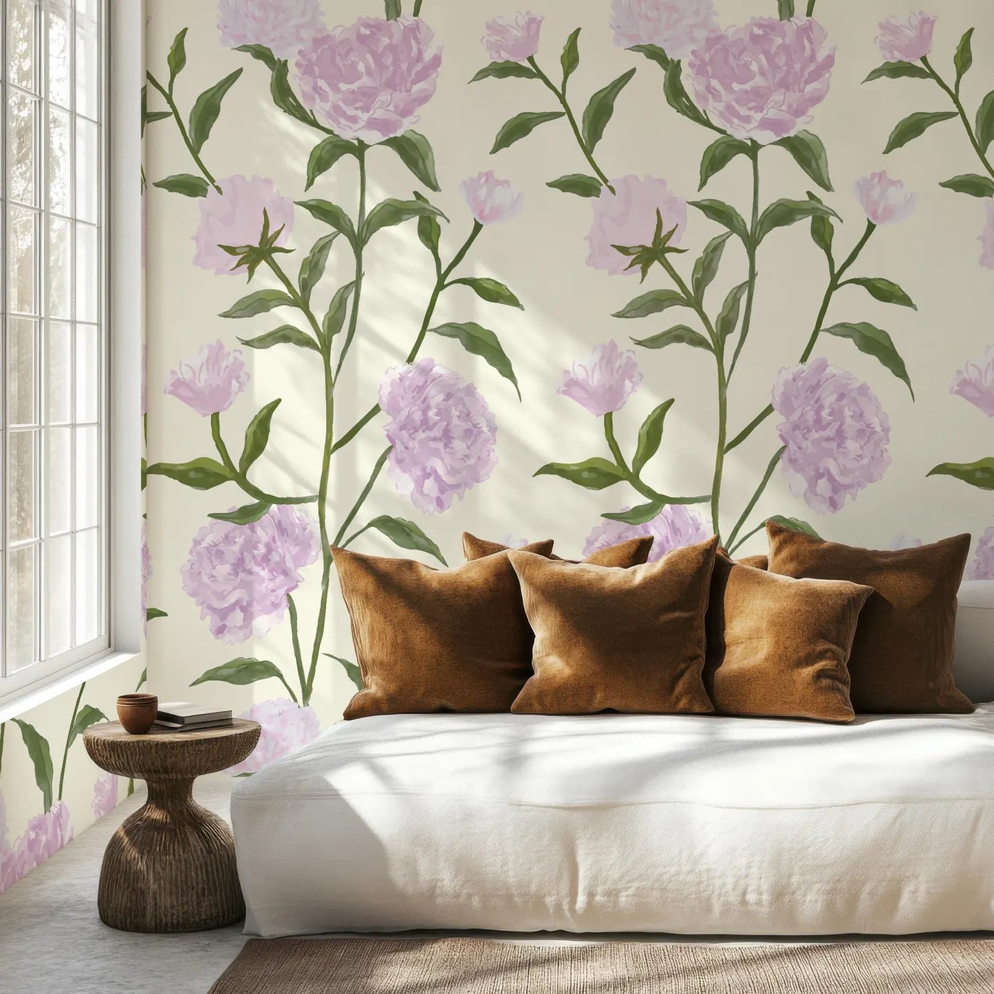 a cozy living room with a white sofa adorned with brown throw pillows. The sofa is positioned against a wall with a floral wallpaper pattern, creating a warm and inviting atmosphere. A small side table is located next to the sofa, providing a convenient space for placing items like books or drinks. The room is well-lit, with natural light coming in from a window, enhancing the overall ambiance of the space.