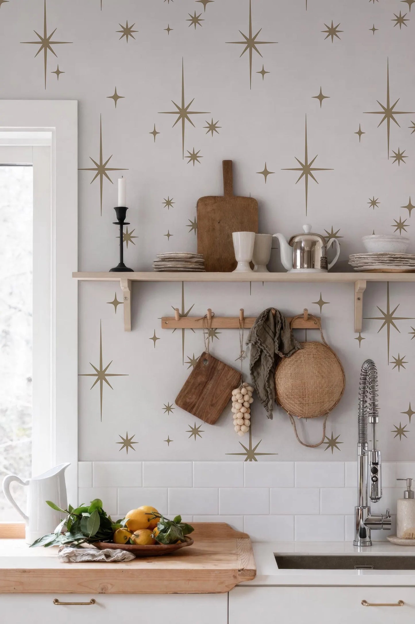 a kitchen with a white countertop, a wooden cutting board, and various kitchen items such as a teapot, a bowl, and a basket. The wall behind the countertop is decorated with a starry pattern, and there are several bowls and cups on the countertop.