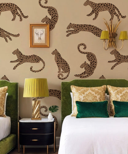 a bedroom with a large wall mural of leopards, a green headboard, and a white bed with green and gold pillows. There is a black nightstand with a lamp and a picture frame on it.