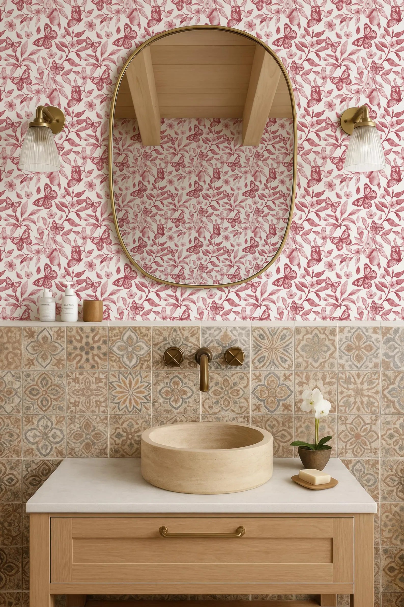 a bathroom with a wooden vanity, a round sink, and a mirror above it. The walls are covered in a pink and white floral wallpaper, and there are two light fixtures on either side of the mirror. The bathroom also includes a small potted plant and a soap dish on the vanity.