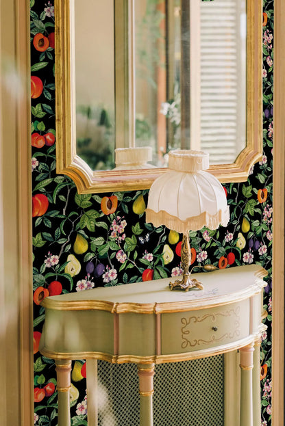 a decorative console table with a lamp and a mirror above it, set against a wall with a vibrant floral wallpaper.