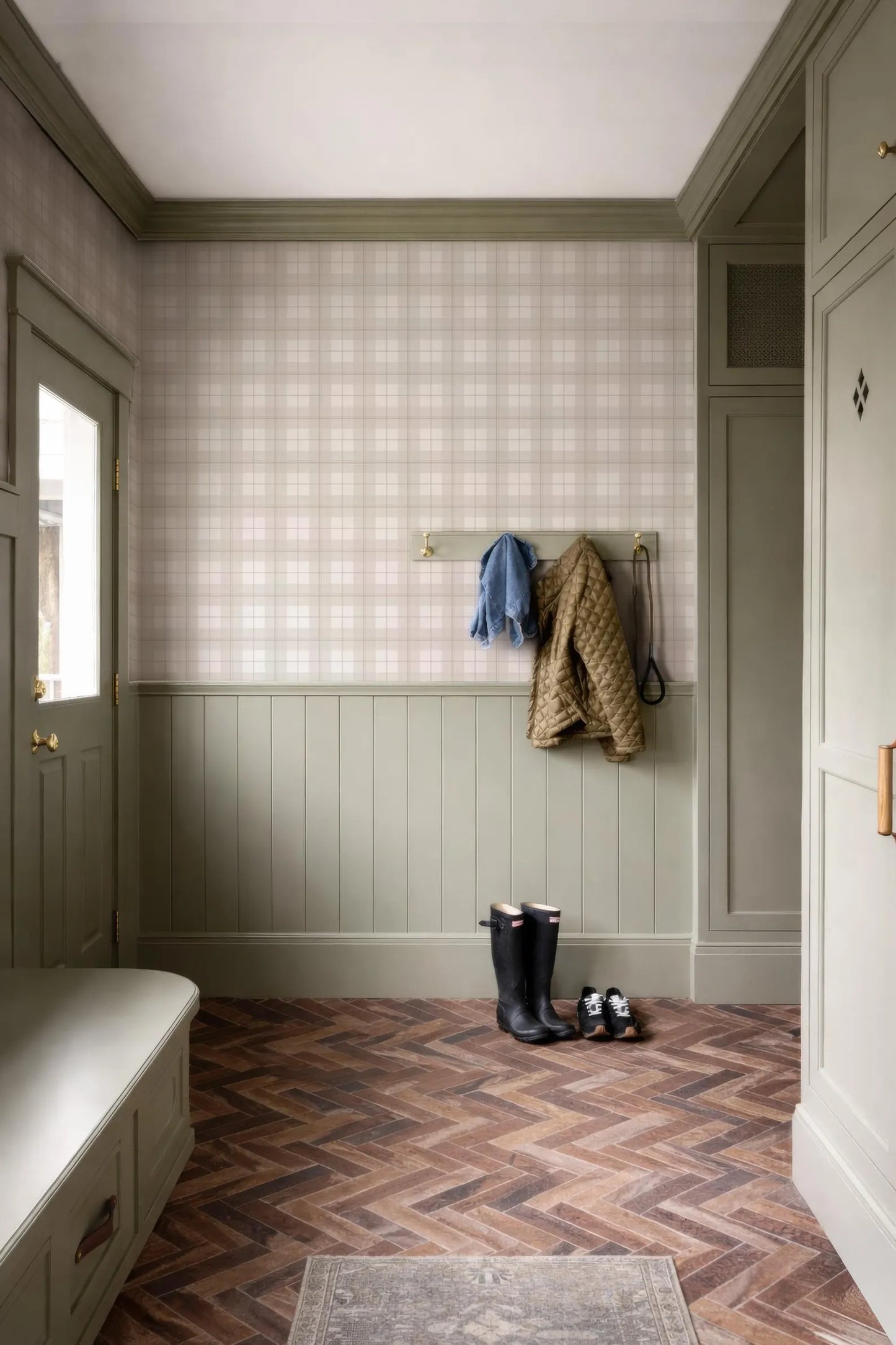 a hallway with a chevron-patterned wooden floor, a coat rack with a jacket and boots, and a window.