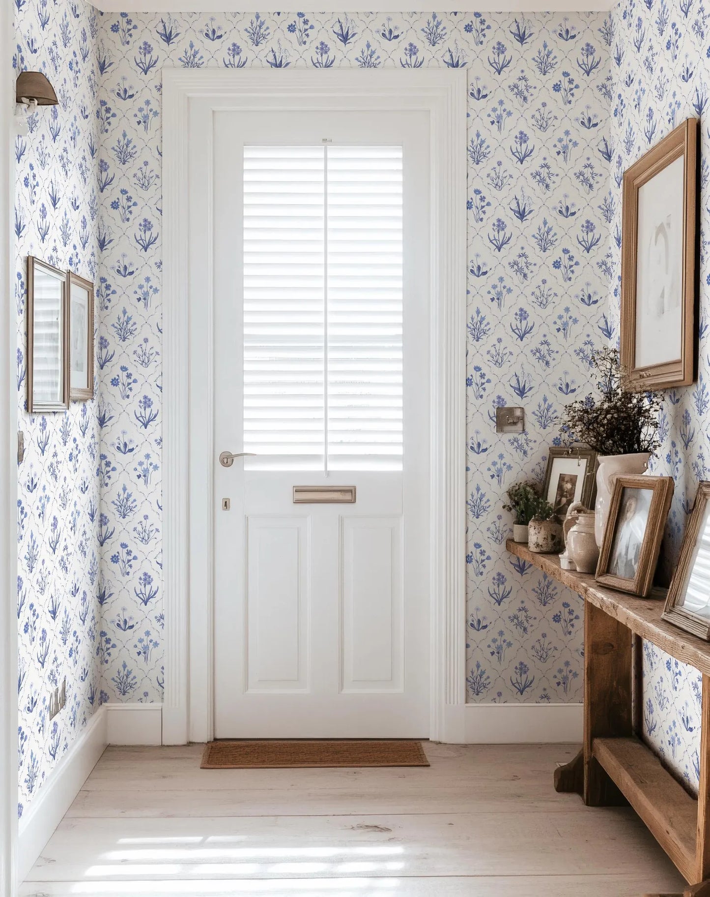 a hallway with a white door, a wooden console table with framed pictures, and a blue and white patterned wallpaper.