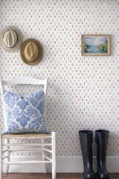 a white chair with a blue and white floral pillow, a pair of black rain boots, and a framed landscape painting on the wall.
