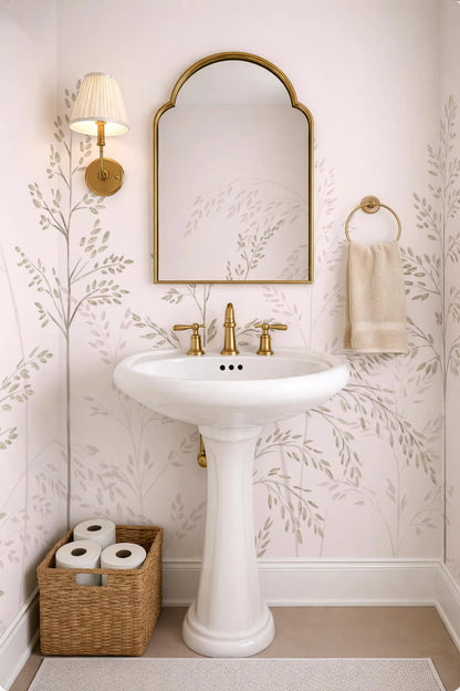 a bathroom with a white pedestal sink, a mirror, and a towel rack. The walls are decorated with a floral pattern, and there is a basket of toilet paper on the floor next to the sink.