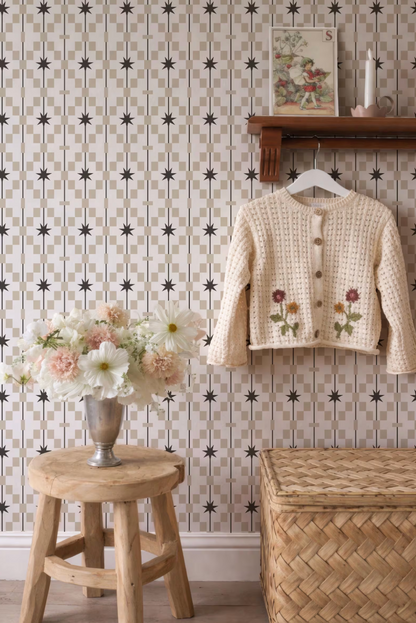 a cozy and charming interior scene with a wooden stool, a vase of flowers, a wooden shelf with a sweater, and a woven basket. The wall behind these items is adorned with a patterned wallpaper, adding a touch of elegance to the space.