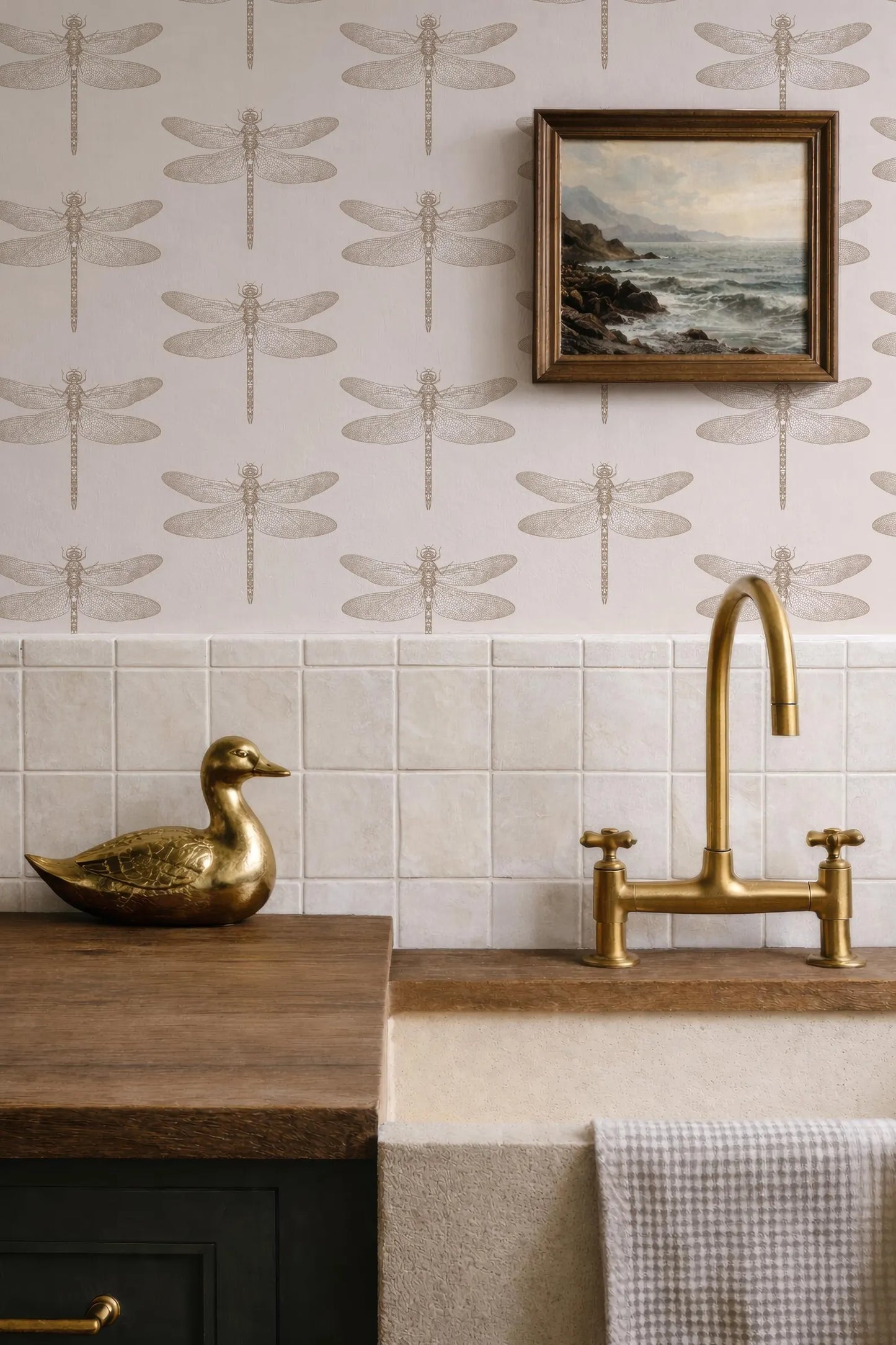 a bathroom with a dragonfly wallpaper, a gold duck figurine on a wooden counter, a gold faucet, and a framed landscape painting above the sink.