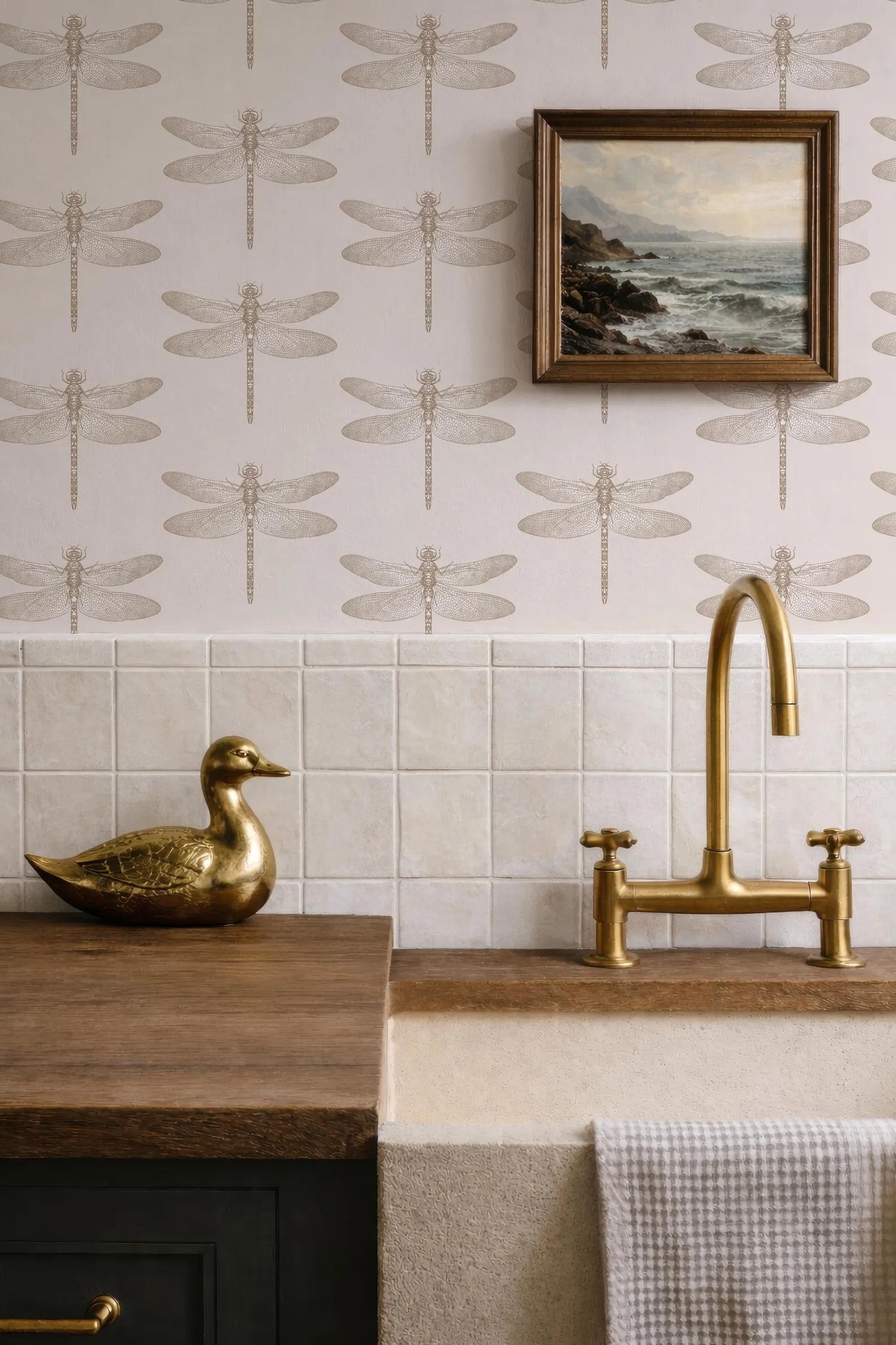 a bathroom with a dragonfly wallpaper, a gold duck figurine on a wooden counter, a gold faucet, and a framed landscape painting above the sink.