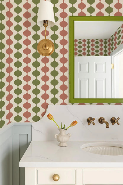 a bathroom with a white sink, a mirror, and a vase of tulips on the countertop. The walls are covered in a patterned wallpaper with a mix of green, red, and white colors. A gold-framed mirror is mounted above the sink, and a light fixture is installed above the mirror.