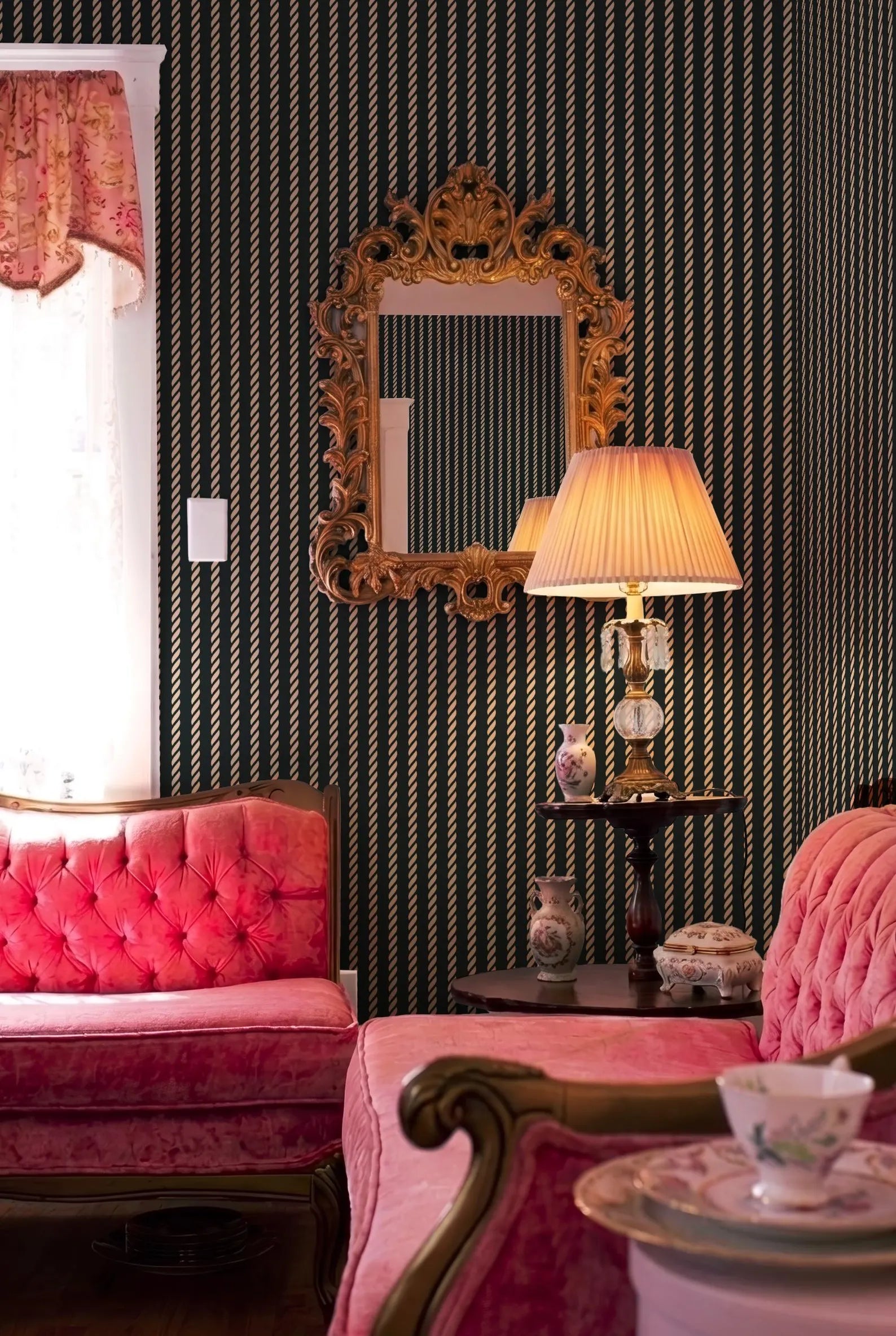 a cozy and elegant living room with a pink tufted sofa, a wooden side table with a lamp, and a large ornate mirror on the wall.