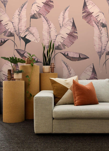 a modern living room with a gray sofa adorned with orange and white throw pillows, a wooden coffee table, and a wallpapered wall with a tropical leaf pattern.
