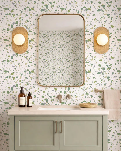 a bathroom with a white and green speckled wall, a white sink, a mirror, and two round wall sconces. The bathroom has a green cabinet below the sink and a beige towel hanging on the right side.