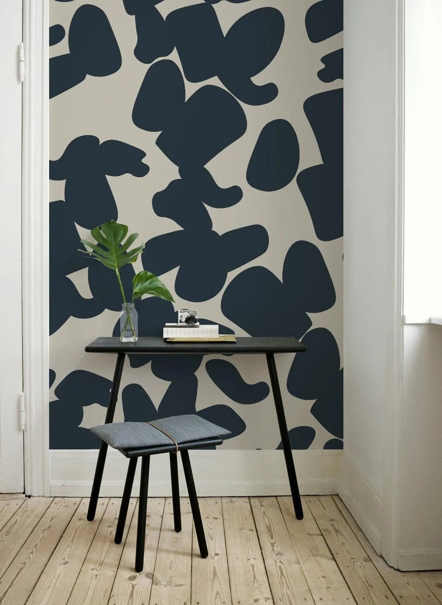 a modern and minimalist interior design with a black and white patterned wall behind a small black desk with a plant and a book on it.