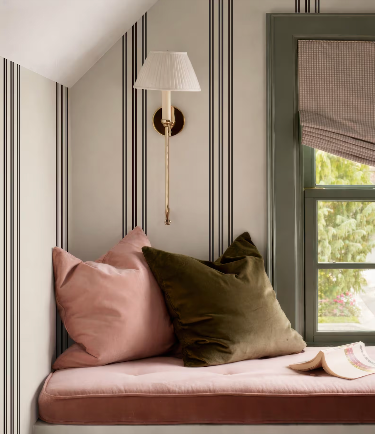 a cozy corner of a room with a window, a lamp, and a comfortable-looking couch with pillows.