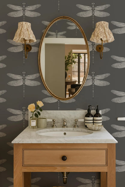 a bathroom with a white marble sink, a wooden vanity, and a large oval mirror with gold frame. The walls are decorated with a dragonfly pattern wallpaper, and there are two lamps with white shades on either side of the mirror.