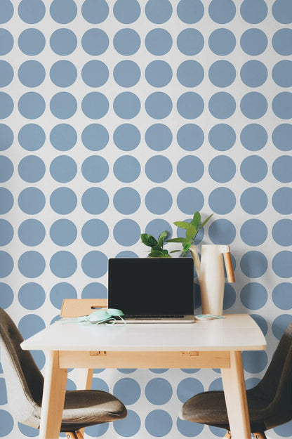 a modern workspace with a white table, a laptop, and a plant. The table is set against a wall with a blue and white polka dot pattern. The workspace is furnished with two chairs, one on each side of the table.