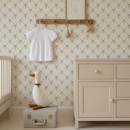 a nursery room with a white dresser, a wooden hanger, and a stuffed duck on a suitcase. The room has a patterned wallpaper and a wooden shelf with a picture frame.