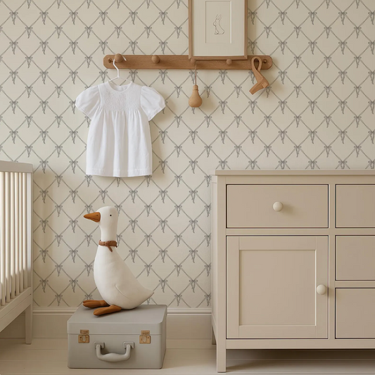 a nursery room with a white dresser, a wooden hanger, and a stuffed duck on a suitcase. The room has a patterned wallpaper and a wooden shelf with a picture frame.