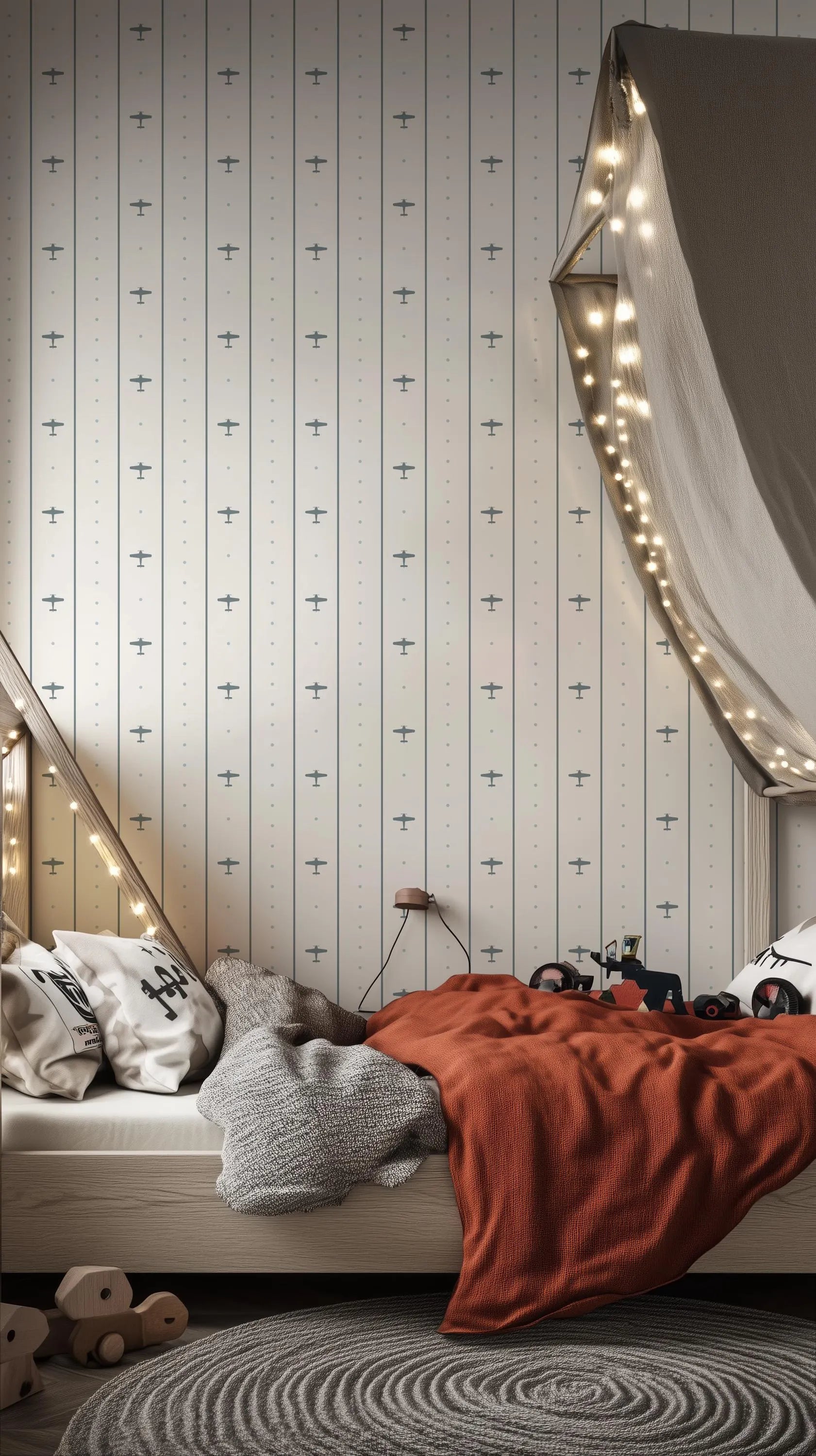 a cozy bedroom scene with a bed, a gray blanket, and a red blanket. The bed is covered with a gray blanket and has a wooden headboard. The walls are decorated with a striped wallpaper featuring small airplane designs. The room also has a canopy and string lights, creating a warm and inviting atmosphere.