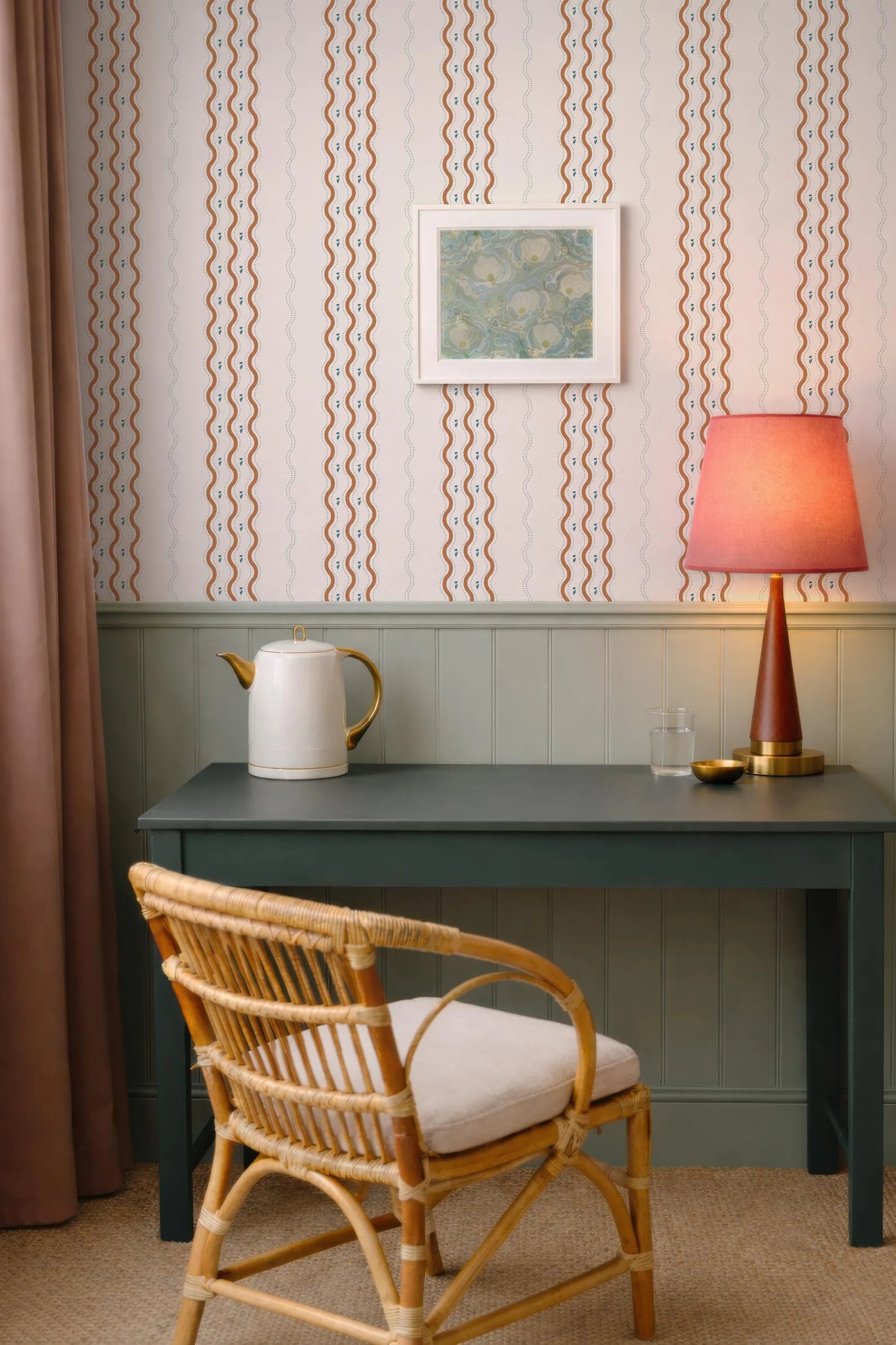 a cozy corner of a room with a wicker chair, a small table with a lamp, and a framed picture on the wall.