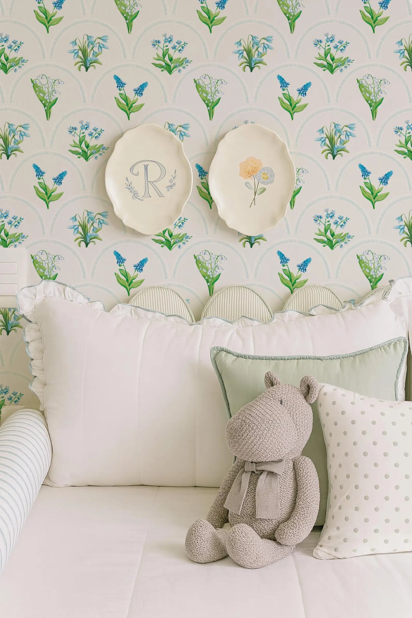 a cozy bedroom scene with a plush stuffed animal, a white bed with decorative pillows, and a wallpapered wall with floral patterns.