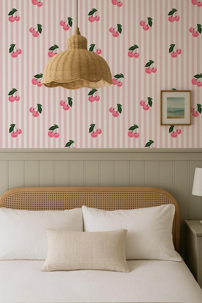 a bedroom with a bed, a wicker pendant light, and a framed picture on the wall. The wall has a pink and white striped pattern with cherries printed on it.
