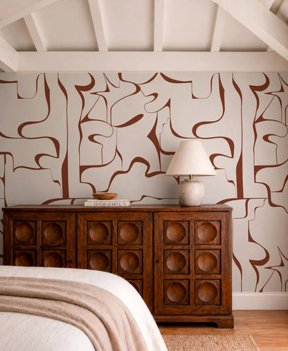 a bedroom with a wooden dresser and a lamp on top. The dresser has a wooden design with circular cutouts, and the lamp has a white shade. The walls are decorated with abstract patterns in shades of brown and white.