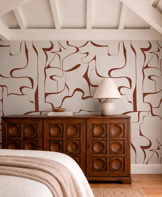a bedroom with a wooden dresser and a lamp on top. The dresser has a wooden design with circular cutouts, and the lamp has a white shade. The walls are decorated with abstract patterns in shades of brown and white.