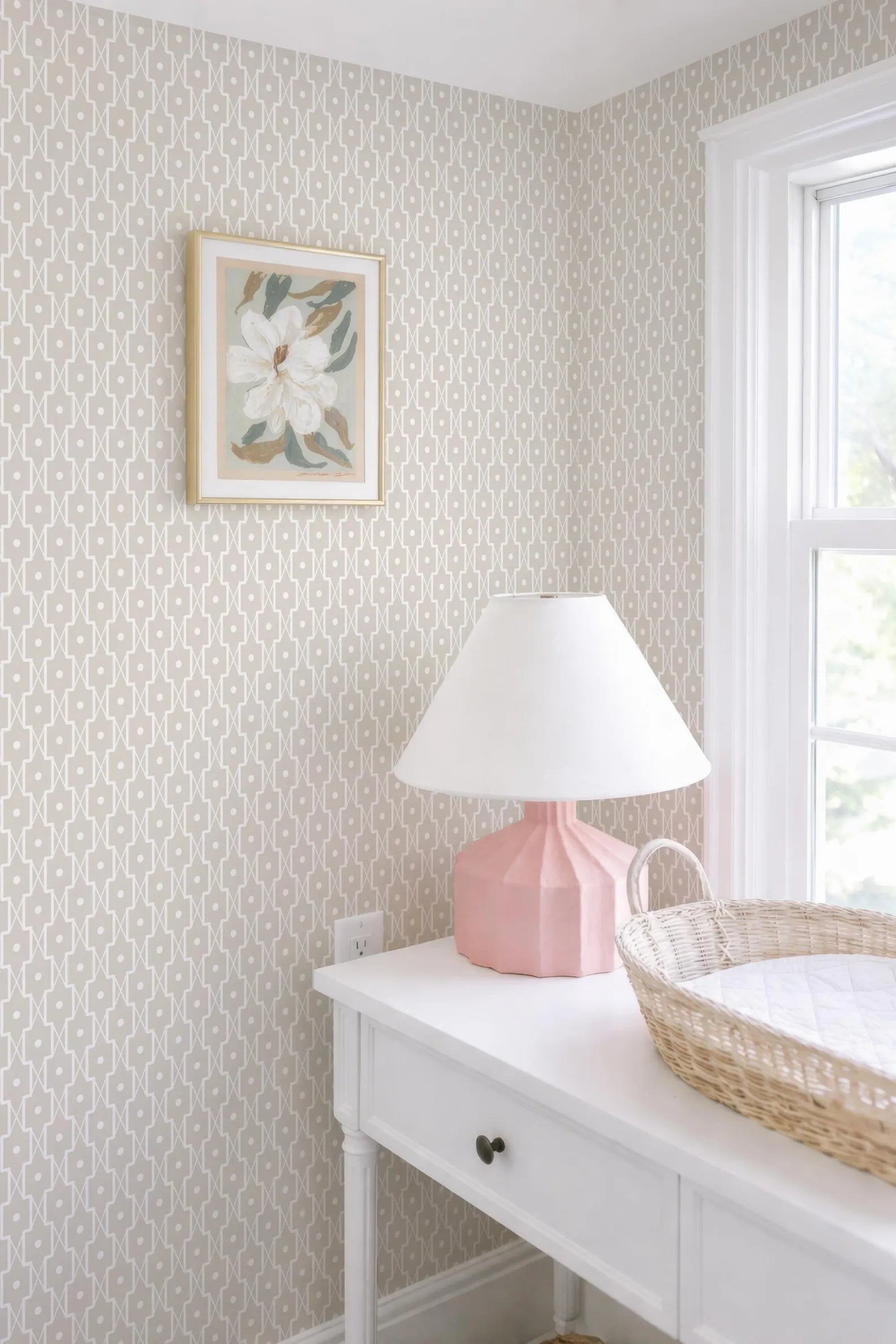 a white dresser with a pink lamp and a woven basket on top, situated next to a window.