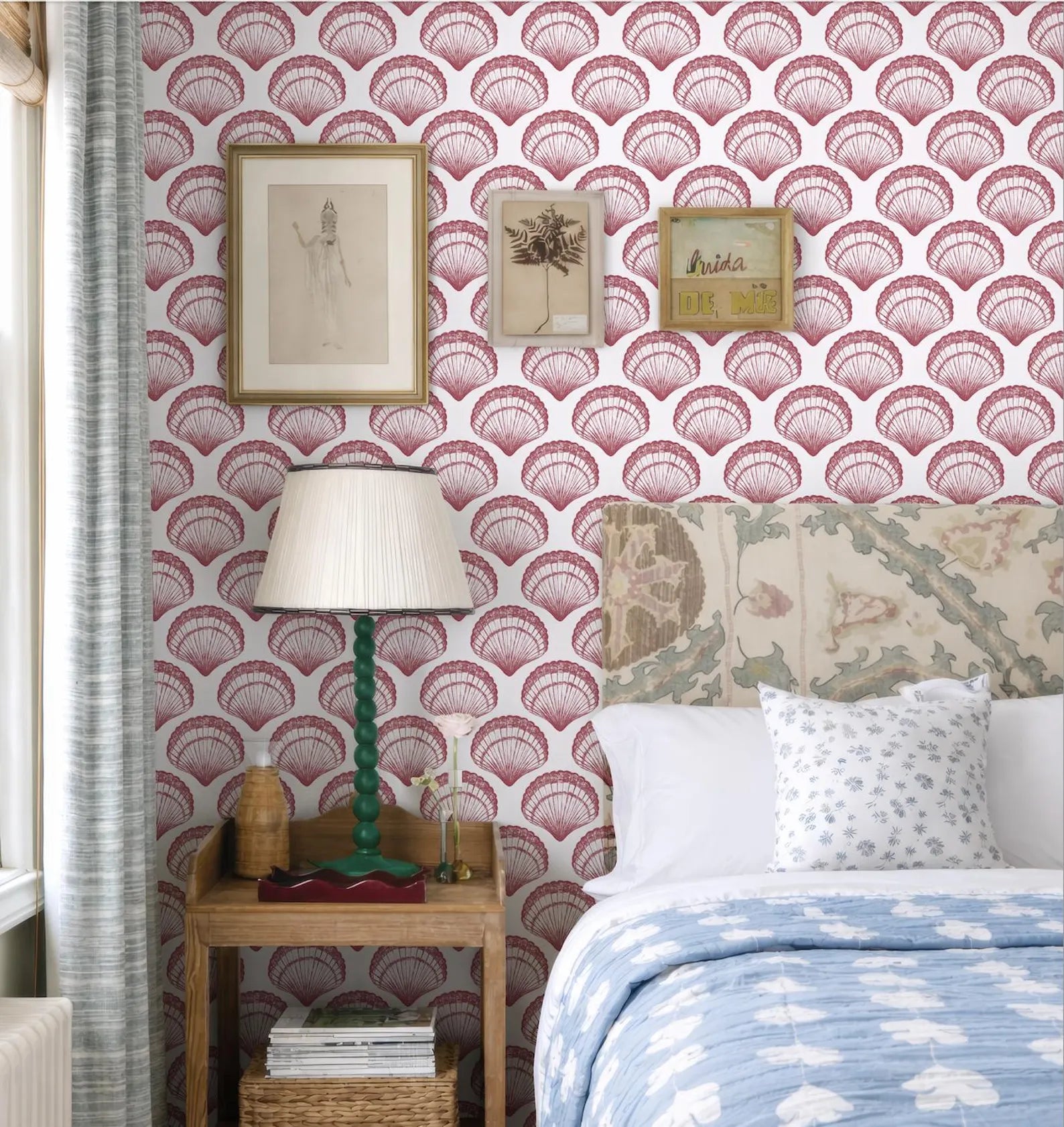 a bedroom with a bed, a nightstand, and a lamp. The walls are decorated with a patterned wallpaper, and there are framed pictures and a lamp on the nightstand.