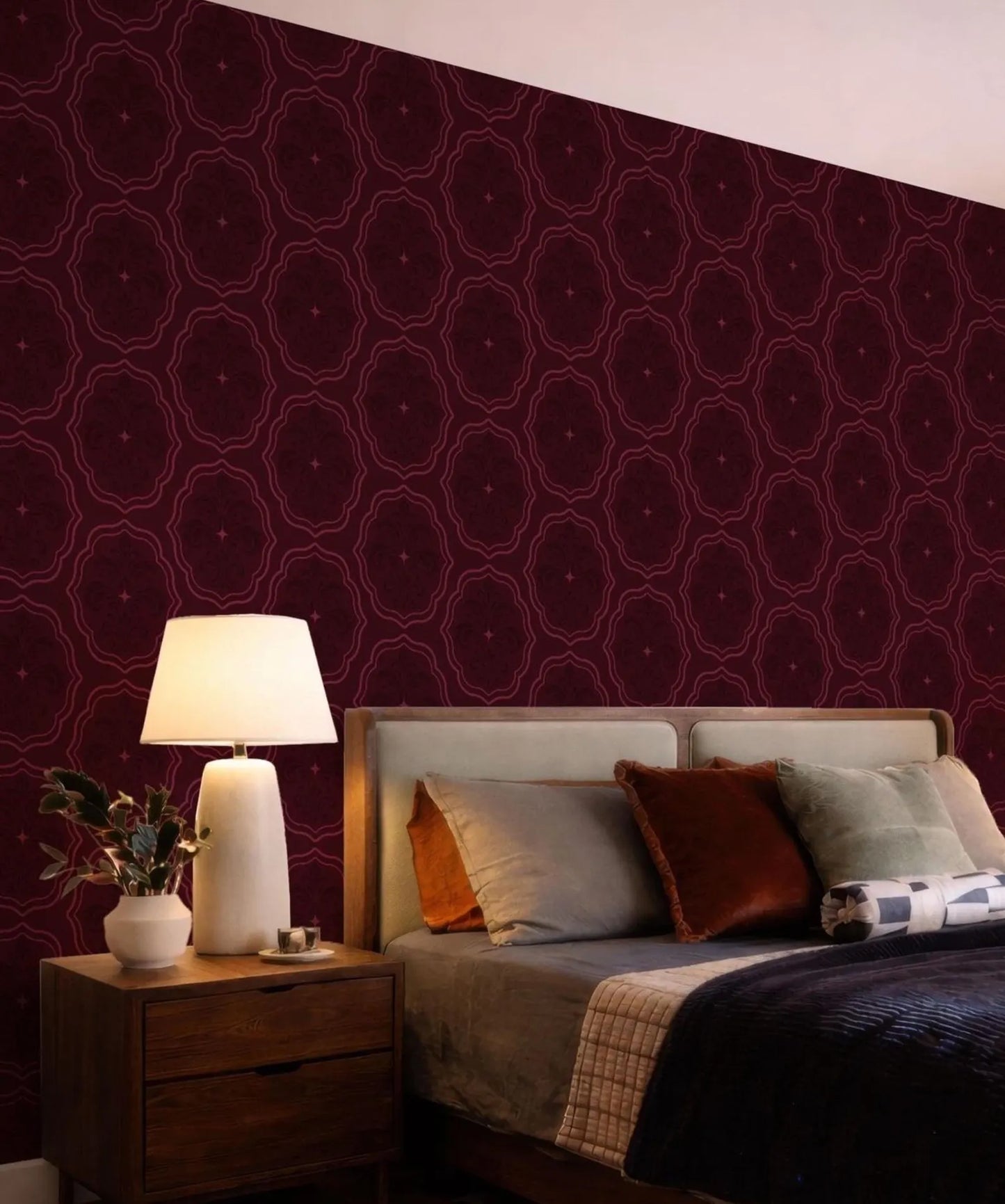 a bedroom with a bed, a nightstand, and a lamp. The walls are covered in a patterned wallpaper in a burgundy color.