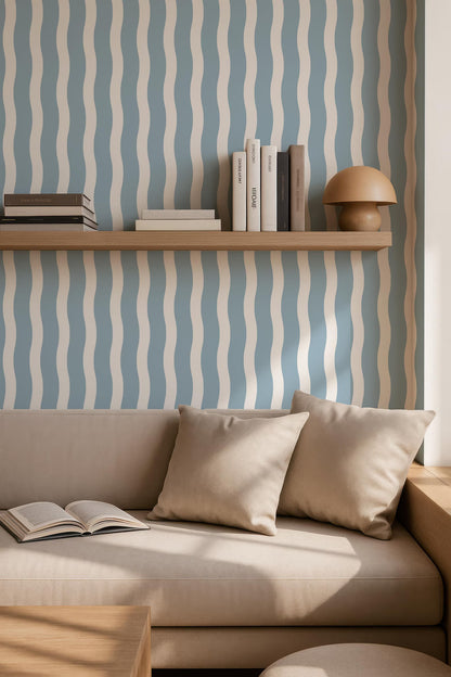a cozy living room with a beige sofa, a wooden side table, and a bookshelf with several books. The wall behind the sofa has a blue and white striped pattern, adding a vibrant touch to the room.