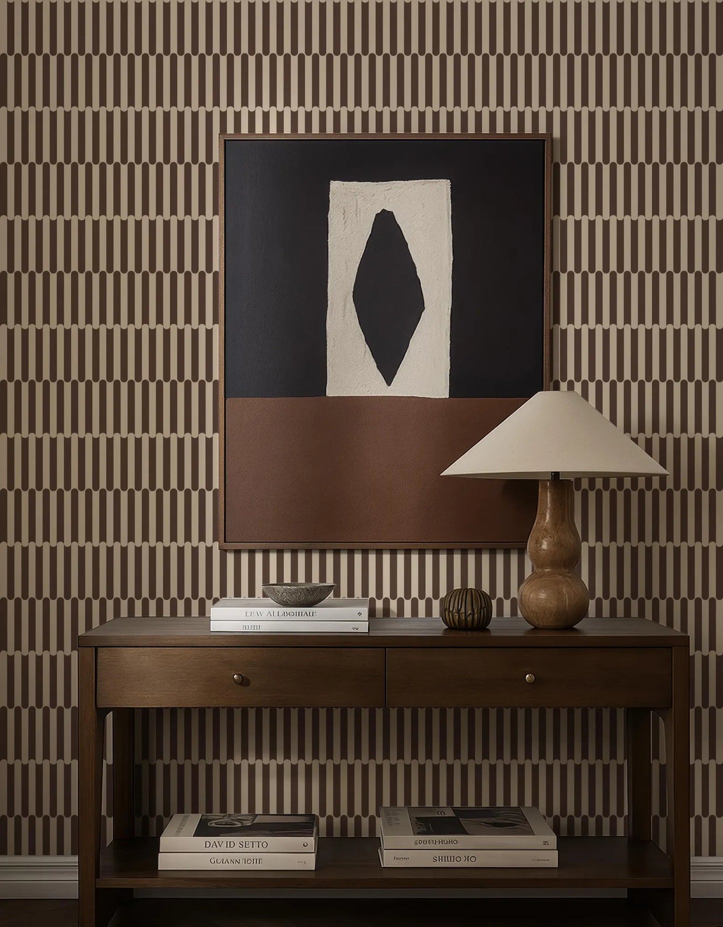 a wooden console table with a lamp, books, and a framed abstract artwork on the wall above it.