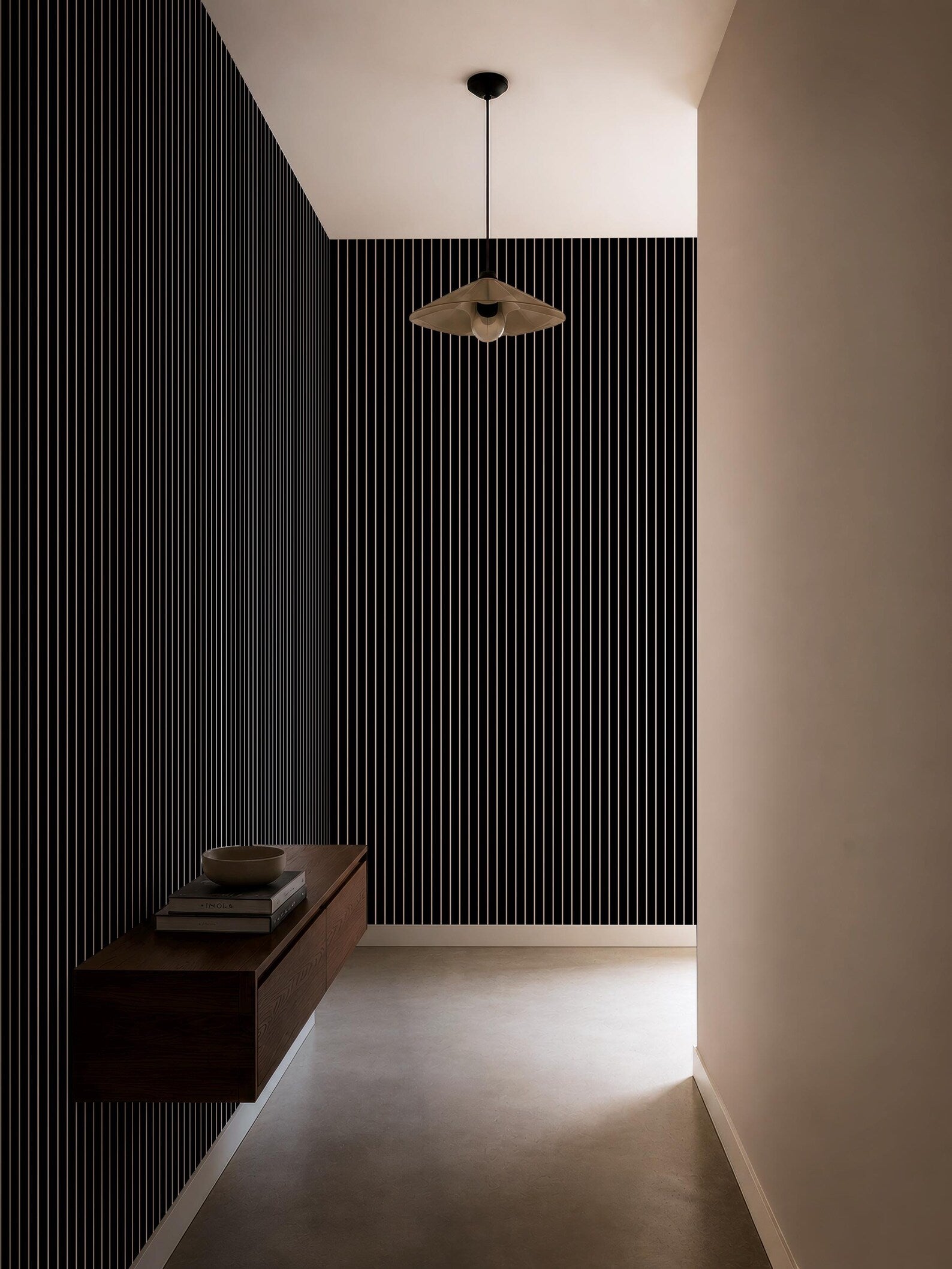 a minimalist hallway with a black and white striped wall, a wooden shelf, and a hanging light fixture.