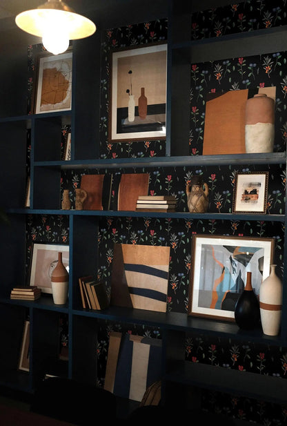 a dark blue bookshelf filled with various decorative items, including vases, books, and framed pictures. The bookshelf has a floral pattern on the wall behind it, adding a touch of elegance to the overall design.