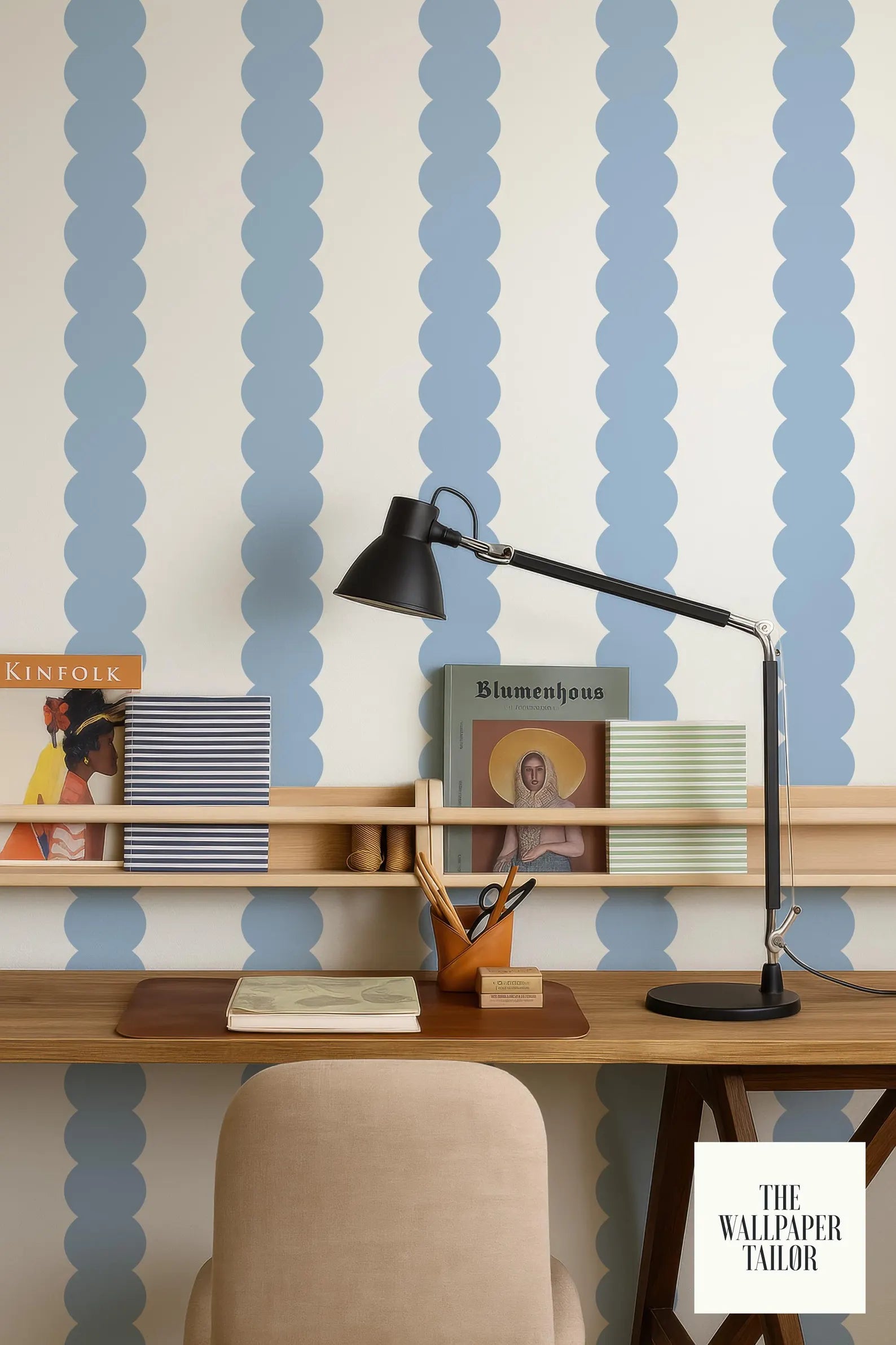 a wooden desk with a lamp, books, and a magazine rack, set against a blue and white striped wallpaper.