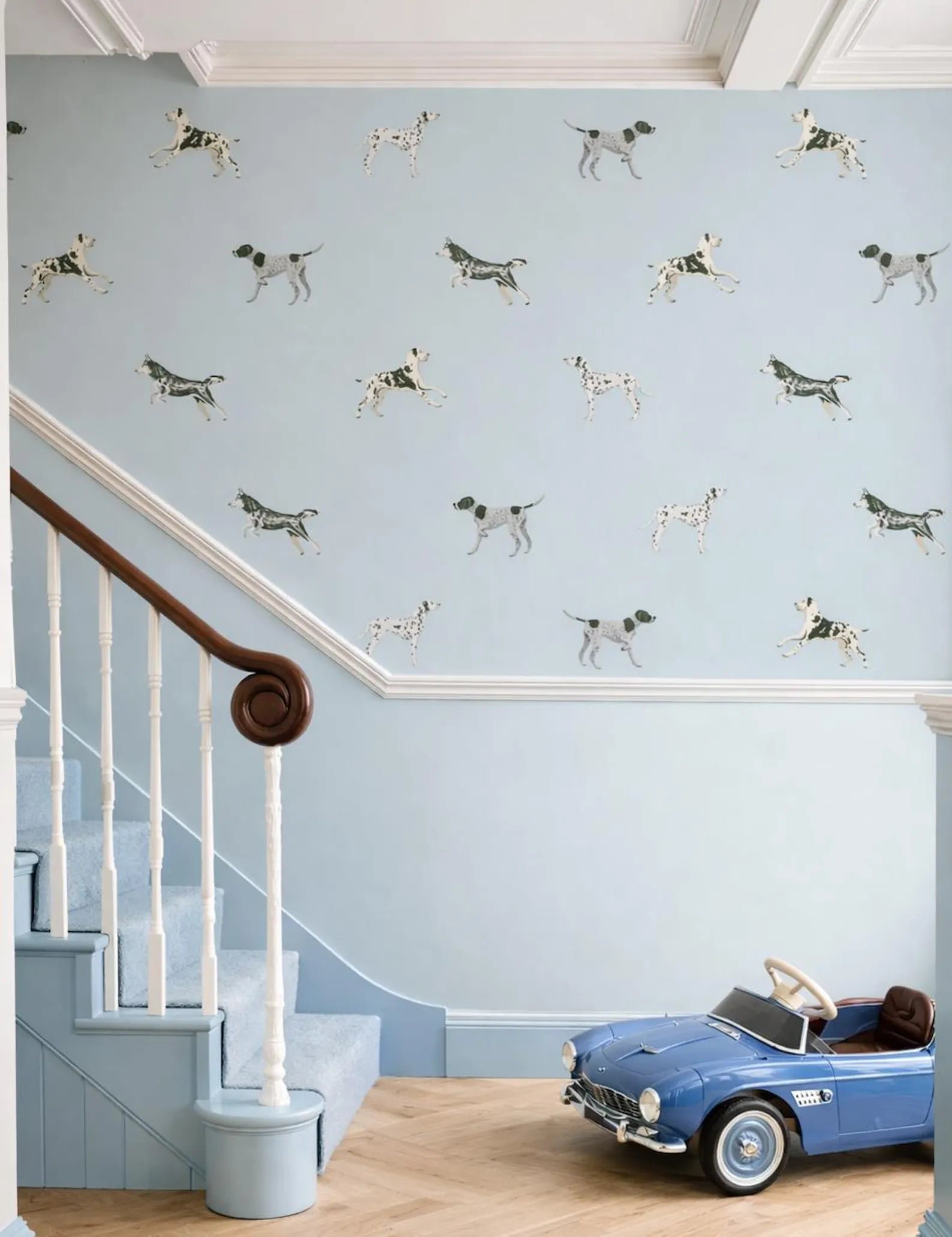 a blue staircase with a pattern of black and white dogs on the wall behind it, and a blue toy car is parked on the floor next to the stairs.