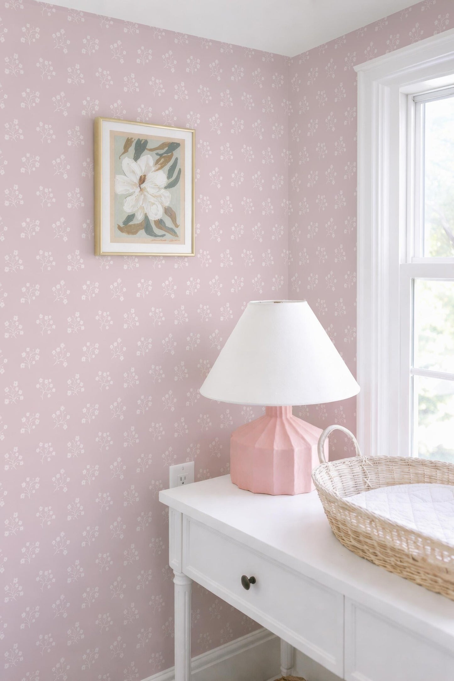 a white dresser with a pink lamp, a white picture frame, and a woven basket on top.