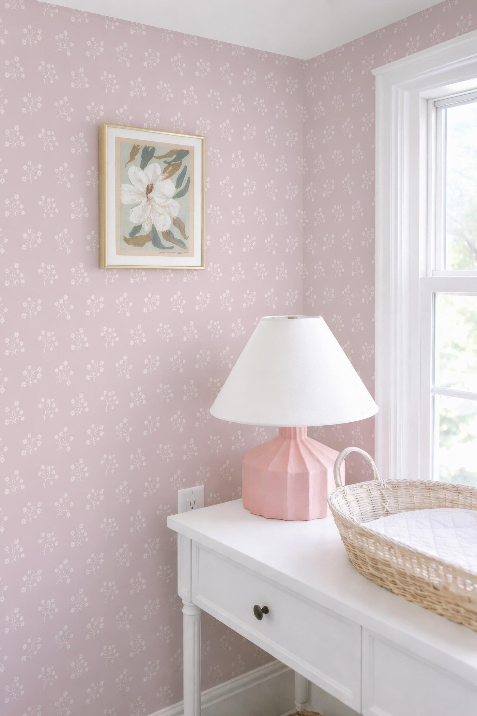 a white dresser with a pink lamp, a white picture frame, and a woven basket on top.