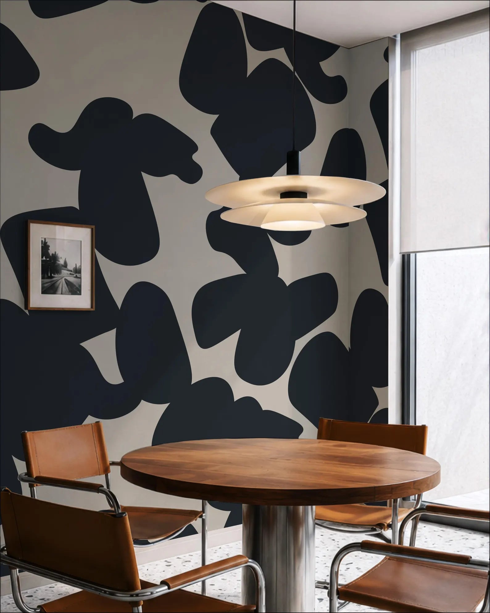 a modern dining room with a round wooden table and four chairs. The walls are decorated with a black and white abstract pattern, and a pendant light hangs above the table.